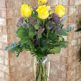 Yellow roses with purple filler in a clear glass vase