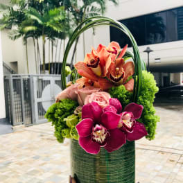 Orchid and rose arrangement in a green cylindrical container with a loop handle