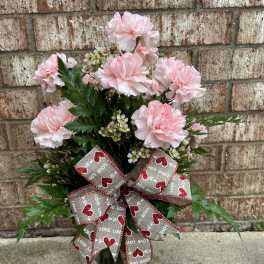 Pink carnations arranged with greenery and a heart-patterned ribbon bow.