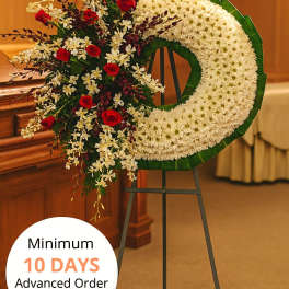 Large white crescent funeral wreath with red roses and white orchids on a metal easel stand.