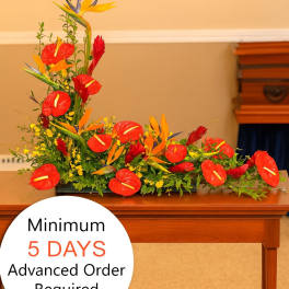 Tropical funeral spray with red and orange flowers arranged low on a wooden table