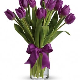 Purple tulips in a clear glass vase with a purple ribbon
