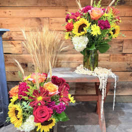 Two colorful flower arrangements in green glass vases with wheat accents