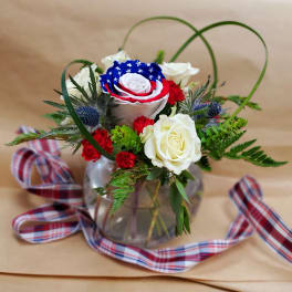 Red, white, and blue rose arrangement in a glass vase with plaid ribbon