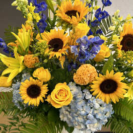 Bright bouquet of sunflowers, yellow roses, blue hydrangeas, and lilies in a white vase