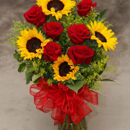 Bouquet of red roses and yellow sunflowers in a glass vase with a red ribbon