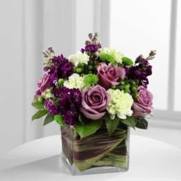 Purple and white floral arrangement in a square glass vase