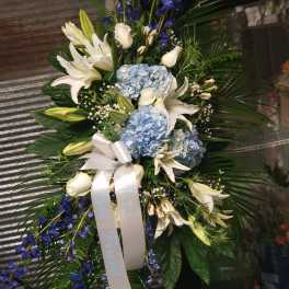 Standing floral spray with white lilies, blue hydrangeas, and blue ribbon