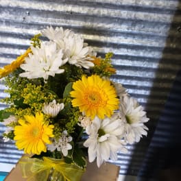 Yellow and white daisy bouquet in a glass jar with a yellow ribbon