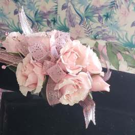 Pink rose corsage with glittery ribbon on a black display stand