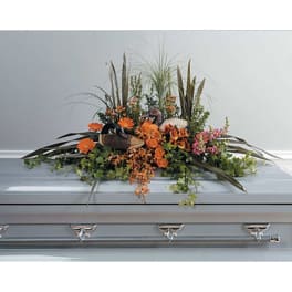 Orange floral casket spray with greenery on a silver casket
