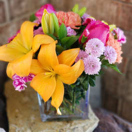 Colorful bouquet with yellow lilies, pink roses, and lavender mums in a glass vase