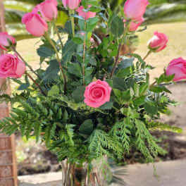 Tall arrangement of pink roses with lush greenery in a clear glass vase