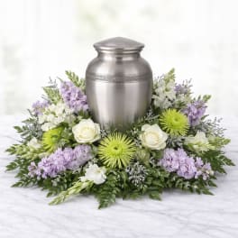 Funeral urn surrounded by white, lavender, and green flowers