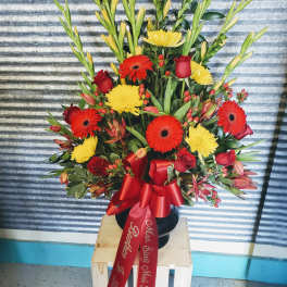 Tall floral arrangement with red roses, gerbera daisies, and yellow blooms in a black vase