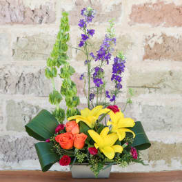 Yellow lilies and orange roses in a rectangular vase with purple spikes