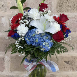 Bouquet of red roses, white lilies, and blue hydrangeas in a glass vase