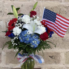 Bouquet of red, white, and blue flowers in a glass vase with an American flag