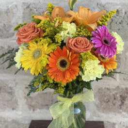 Mixed bouquet of orange, pink, and yellow flowers in a glass vase