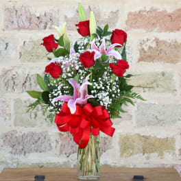 Bouquet of red roses and pink lilies in a clear glass vase with a red bow