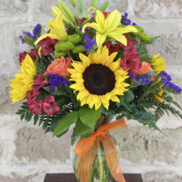 Bright mixed bouquet with sunflowers, lilies, and roses in a glass vase