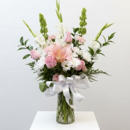 Pink and white flower arrangement in a glass vase with a white ribbon