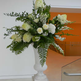 Tall white floral arrangement in a pedestal vase with roses and hydrangea