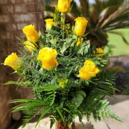 Yellow roses arranged in a glass vase with fern foliage