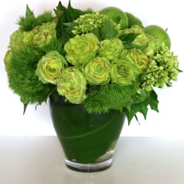 Green floral arrangement in a glass vase with round blooms and apples