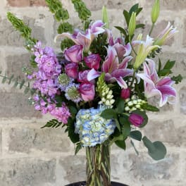 Mixed bouquet of pink lilies, roses, hydrangea, and lavender flowers in a glass vase