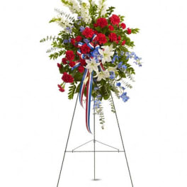Standing floral spray with red carnations, white lilies, and blue flowers on an easel