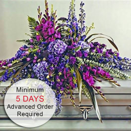 Long purple and pink floral casket spray arranged on a silver casket.