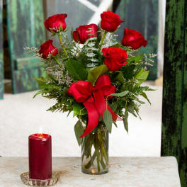 Red roses in a glass vase with a red ribbon, beside a lit red candle