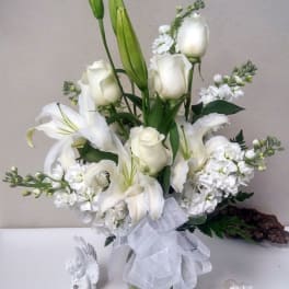 White lilies and roses arranged in a glass vase with a sheer ribbon