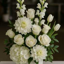 White floral arrangement in a white vase with roses, dahlias, hydrangea, and snapdragons
