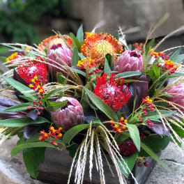 Mixed tropical bouquet in a wooden box with pink protea and red-orange blooms