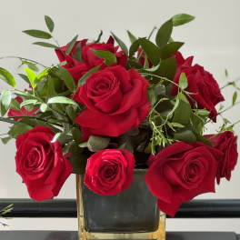 Red roses arranged in a square glass vase with greenery