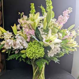 Tall bouquet of white lilies, pink blooms, and green hydrangea in a glass vase