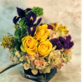 Yellow roses and purple irises in a square glass vase