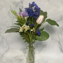 Mixed bouquet of blue, lavender, and white flowers in a clear glass vase