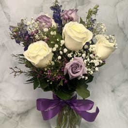 Bouquet of cream and lavender roses in a glass vase with a purple ribbon