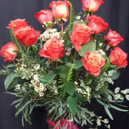 Red roses arranged in a glass vase with greenery and a pink ribbon