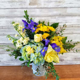 Bouquet of yellow roses, blue irises, and mixed blooms in a metal bucket