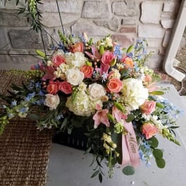 Large pastel floral arrangement with roses, lilies, and hydrangeas in a black container