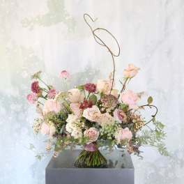 Loose hand-tied bouquet of blush and mauve roses with airy accent flowers and sculptural wire detail.