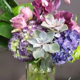 Tall glass vase arrangement with purple orchids, blue hydrangeas, pink roses, and succulents