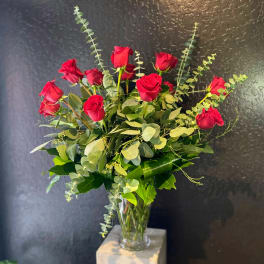 Red roses arranged in a clear glass vase with eucalyptus foliage