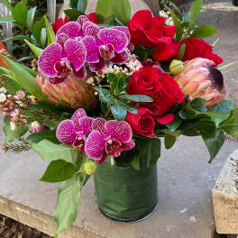 Bouquet of red roses and purple orchids in a green glass vase