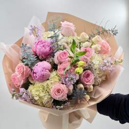 Hand-tied bouquet of pink roses, peonies, and hydrangeas in blush wrap