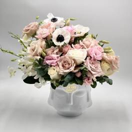 Low pastel arrangement of roses, anemones, and orchids in a white ceramic face vase